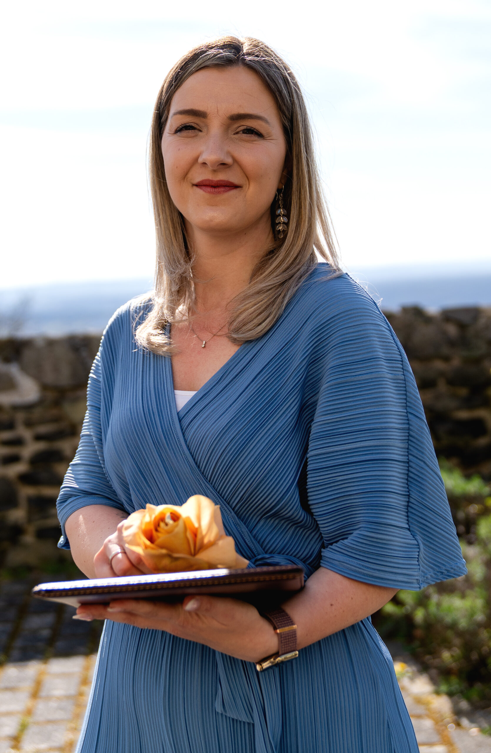 Janine Rhode, Traurednerin für freie Trauung in Hamburg, bei einer Zeremonie im Freien mit Notizmappe und Blume in der Hand, vor maritimer Kulisse.
