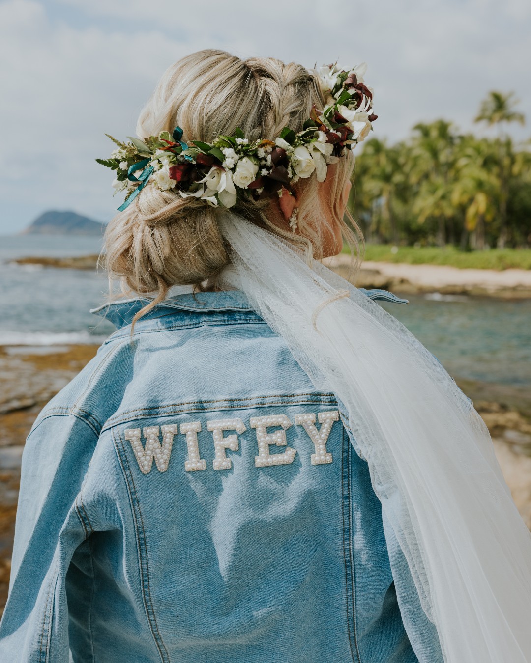 freie Traurednerin Janine1 Braut mit Blumenkranz und Jeansjacke mit 'Wifey'-Schriftzug am Strand von Hawaii – eine moderne Note voller Persönlichkeit und Aloha-Spirit